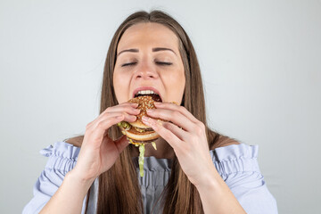 Portrait of a beautiful young woman eating a burger, close up, eyes closed, isolated on white background