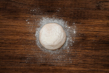 Ball of pizza dough on a rustic wooden background with dusting of flour