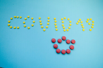 volumetric inscription of multi-colored pills on a blue paper background coronavirus. The crown is made of pink convex tablets for inscription. medicines for the treatment of viral infections