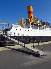 Close-up of merchant ship gangway with original yellow and red funnel or chimney under deep blue...