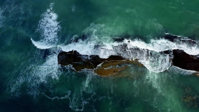 Beautiful bird's eye top aerial drone shot of waves crushing into a black rock in the beach at Sibauma creating a natural swimming pool during low tide near Pipa in Northern Brazil.