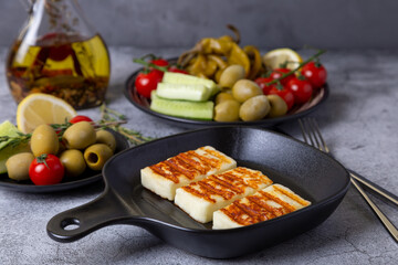 Grilled haloumi cheese on a black pan with olives, tomatoes, cucumbers and pepperoni. Close-up.