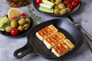 Grilled haloumi cheese on a black pan with olives, tomatoes, cucumbers and pepperoni. Close-up.