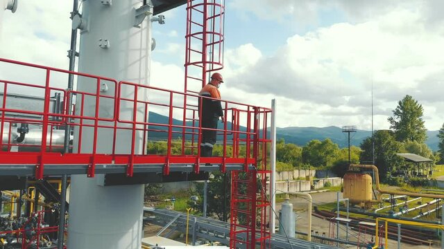 Aerial view gas station operator climbs to the top of the station. Modern gas complex in the mountains. A gas worker climbs the ladder of the gas distribution unit against the backdrop of mountainous