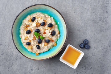 Bowl of oatmeal porridge with almond flakes, blueberries, raisins, honey