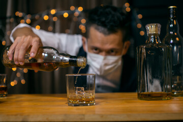 Barman pouring whiskey wearing  protective mask on the bar counter 