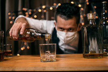 Barman pouring whiskey wearing  protective mask on the bar counter 