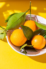 Whole oranges witl orange tree leaves on yellow background