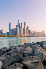 Fototapeta premium Modern buildings of Dubai Marina view from Palm Jumeirah beachside with pink skies during sunset