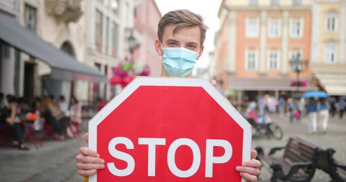 People's lives during the epidemic and quarantine. Stop epidemic! A young man in a mask and with a stop sign in his hands stands on the street where many people do not comply with quarantine and socia