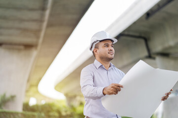 Portrait engineer handsome man or architect looking construction with blueprint and white. helmet in construction site.