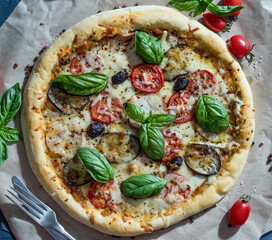 Pizza with basil, bacon, tomatoes and cheese on paper lies on a table with a knife and fork