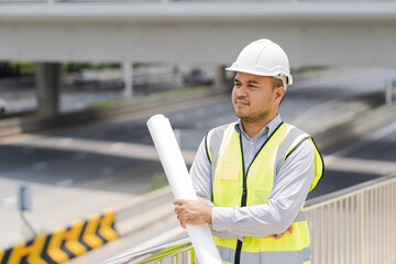 Portrait engineer handsome man or architect looking construction with blueprint and white safety  helme in construction site.