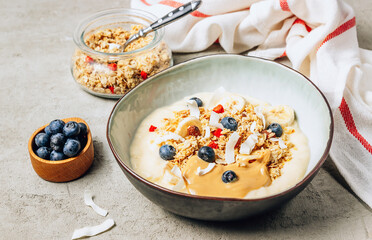 Morning healthy breakfast bowl with yogurt, muesli, blueberry, banana, coconut on the concrete background.