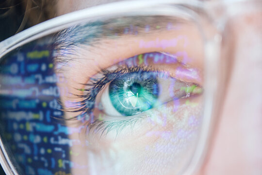 Close up of blue hacker eye with Glasses. Reflection of computer code in glasses. Focused on work Software developer looking at the computer. Hacking, vision and technology concept 