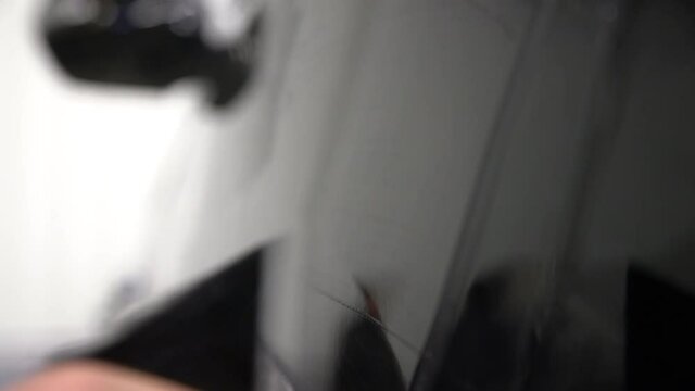 Extreme close-up of using a squeegee and spray to apply a clear plastic paint protection film to the side of a black car.