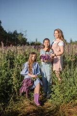 Fototapeta premium Happy mother and two little daughters play outdoors in the summer park. Family lifestyle. Mom is relaxing with the children on the green grass. 