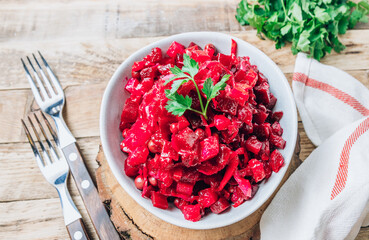 Russian traditional beetroot salad with beetroot, potato, carrot, cucumber, pea and oil dressing. Beet salad on a bowl over wooden background.