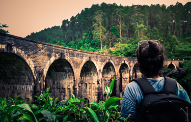 Young woman looks at the Demodara nine arches bridge over the tea plantation in the morning sunlight, the most visited sight of Ella town in Sri Lanka. 