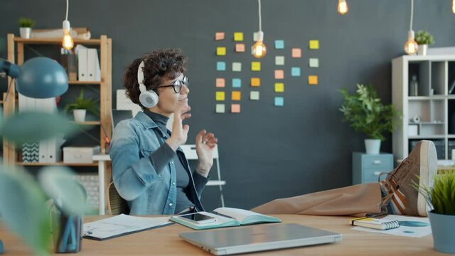 Joyful Girl Office Worker Is Wearing Headphones Dancing In Office Having Fun Alone In Room. Entertainment, Workplace And Youth Culture Concept.