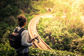 Young woman looks at the Demodara nine arches bridge from above while young couple walking on the bridge in the morning sunlight, the most visited sight of Ella town in Sri Lanka.