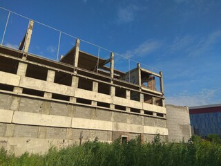  Abandoned concrete building in grey color. Unfinished constructions with the modern building on the background