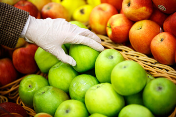 A hand in a protective glove takes an apple from the store counter