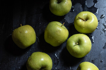 Green apples in drops of water on a black metal board on a background of green grass