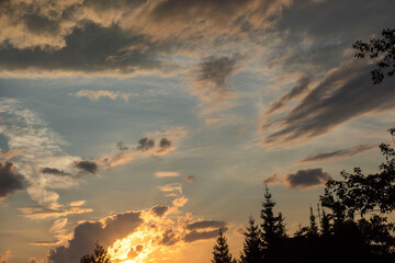 The sun at sunset over the forest bright yellow-orange colors, cumulus clouds of dark black color.