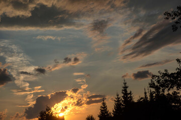 The sun at sunset over the forest bright yellow-orange colors, cumulus clouds of dark black color.