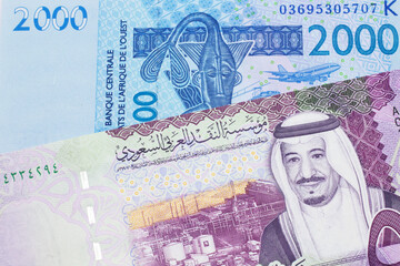 A close up image of a blue, West African franc bank note with a five Saudi riyal bank note in macro