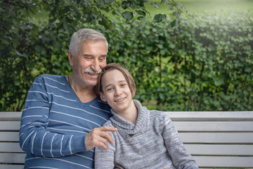 Fototapeta premium portrait of grandfather and grandson, a boy and an elderly man are sitting in a park on a bench, hugging and laughing, come to grandfather for summer vacation