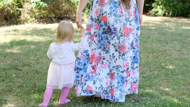 woman in a long dress, mom, teaches you to walk a little kid, a girl with blonde hair on grass in summer, concept of family summer vacation, outdoor games, first steps, child development