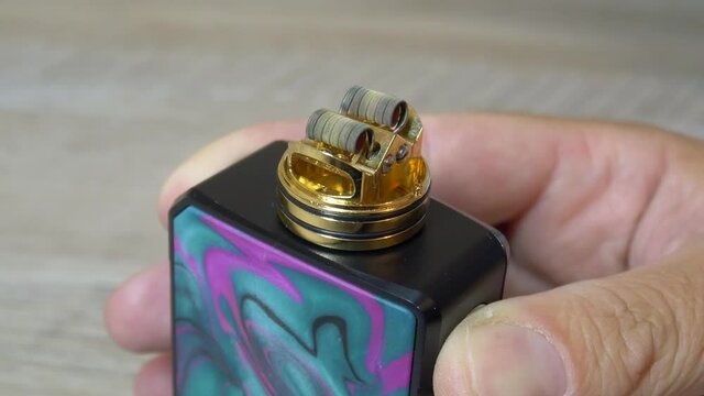 Clapton coil heating in rebuildable dripping atomizer or RDA for vaping. Pressing fire button to heat the coil in vape. Vaping device for quit smoking. 4K macro video with selective focus.