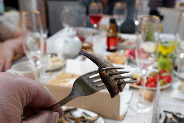   Small fish from a can of sprats strung on a fork, against the backdrop of a festive table.