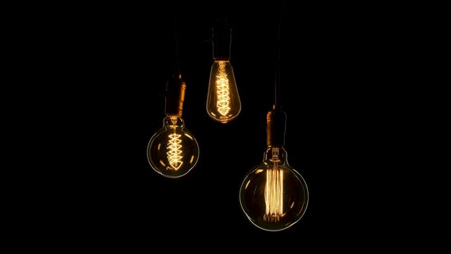 Three different shape retro lamps hang and turn on at the same time on black background. Antique Edison bulbs with old lamp holder are switched on