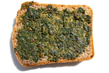 Pesto sauce on one slice of wheat bread isolated on a white background top view.