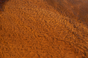 Colorful nature background of yellow red clay bottom. Natural texture of multicolored clay in clear water of mountain creek. Red yellow sandy bottom of mountain river. Full frame of ripples on water.
