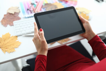 Close-up of woman holding tablet with black screen. Turned off gadget. White desk with creative things for work. Female in red blouse with modern device. Business and technology concept