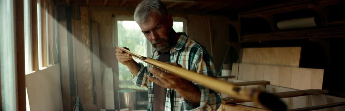 Mid 50s Caucasian male examining a hand made canoe paddle in his workshop. Boat making hobby, small business owner. Shot on RED Dragon