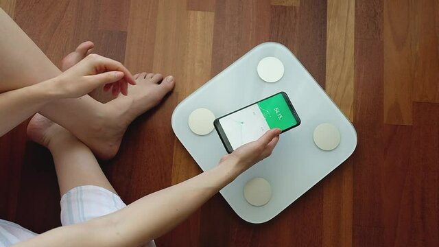 Crop woman using digital weight scales and smartphone application