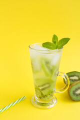 Cold lemonade or infused water with kiwi in the glass  on the yellow background. Location vertical. Copy space.