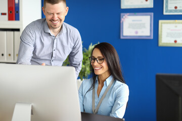 Portrait of smiling worker involved in process. Cheerful middle-aged man and pretty young woman using computer. Blue wall in modern office. Successful business and career concept