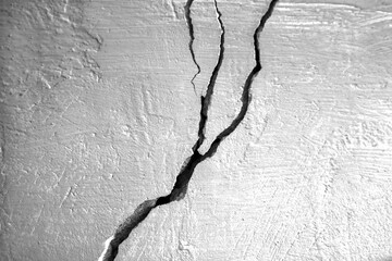 Big branched crack on old concrete wall. Deep crack in wall. Rough stucco painted with gray paint. Horizontal photo. Close-up. Selective focus.