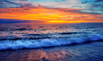 A Colorful Ocean Sunset Sky as a Gentle Wave Rolls to Shore
