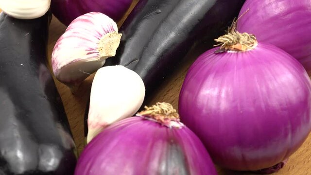 Red onions, eggplants and garlic are laid out on a wooden board, purple vegetable