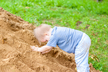 Naklejka na ściany i meble A little boy climbs a mountain with sand. The child is all dirty, but happy. Summer.
