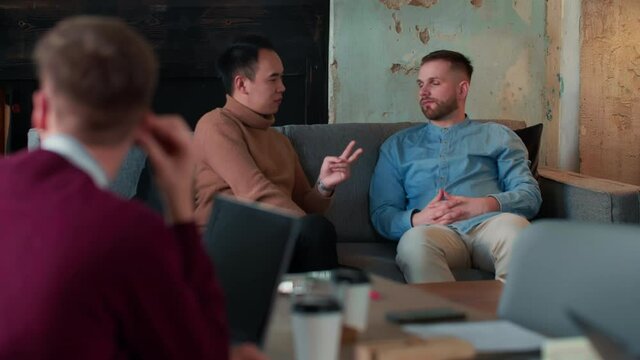Healthy office workplace atmosphere. Two young multiethnic male business people casually chat on couch at coworking.