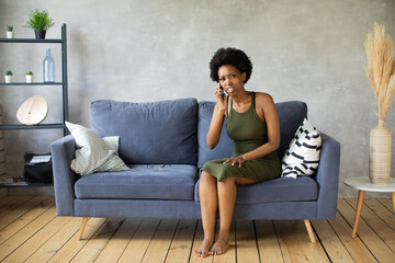Obraz premium Unhappy African American woman talking on the phone, angry girl talking on the phone, discharged or broken mobile device, problem with phone, sitting on sofa