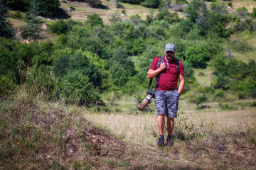 Naklejka premium Nature photographer explores a mountain path. Mountain hiker photographer explores the area for the photographic hunting of wild animals. The man carries the backpack on his shoulders with photography